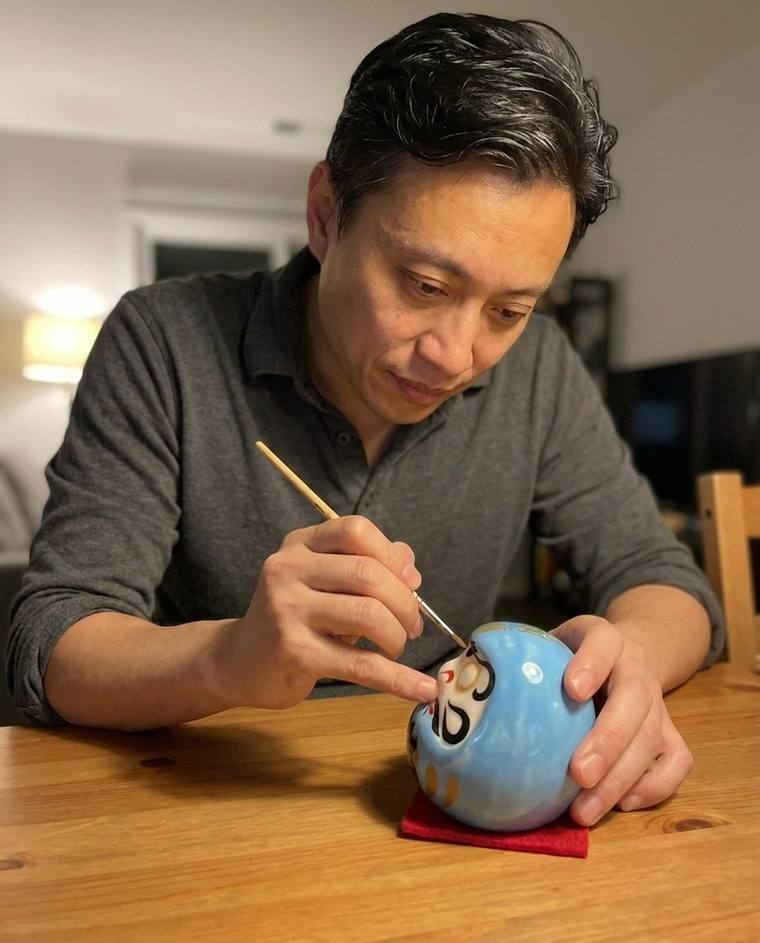 Connor painting the first eye of a blue Daruma at the dining table
