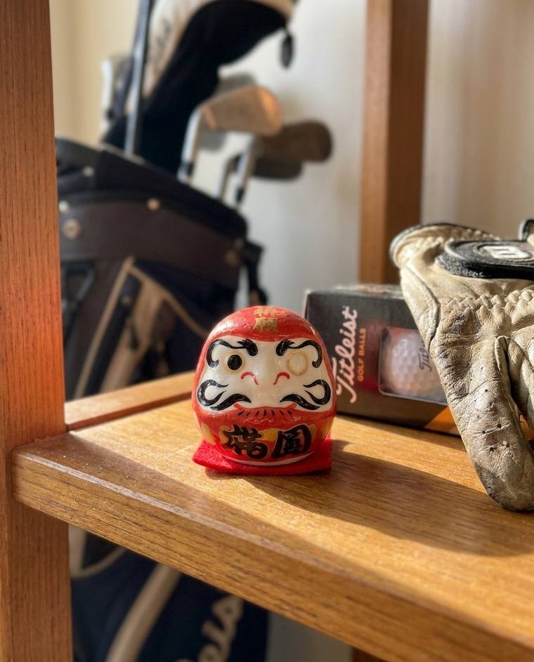 A one-eyed red Daruma on a shelf across from the coffee maker
