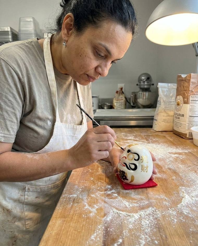 Sarah painting the first eye of a white Daruma at her kitchen sink