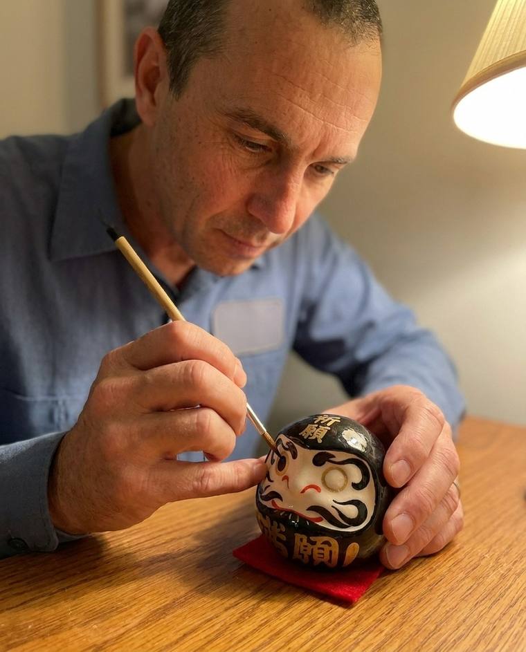 Sean filling the first eye of a black Daruma at his kitchen counter