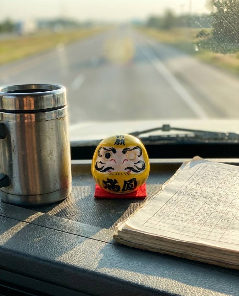 A yellow one-eyed Daruma mounted on the dashboard of Gary's truck