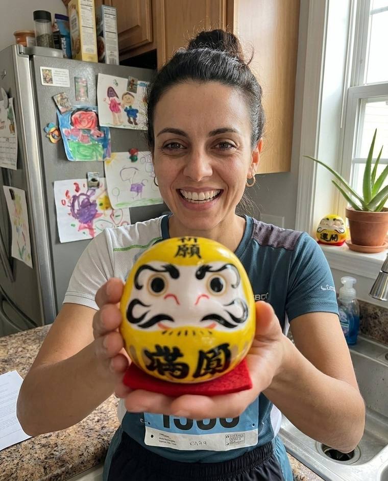 Emily filling in the second eye of the yellow Daruma, still in her race shirt