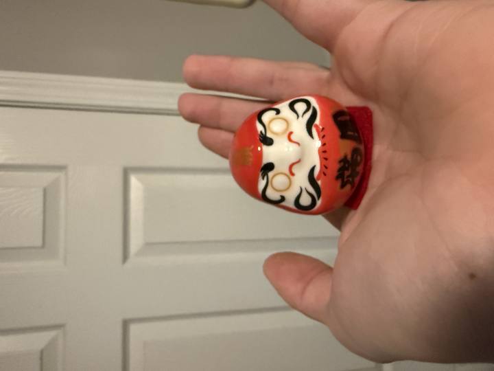 A red ceramic Daruma held in an open hand
