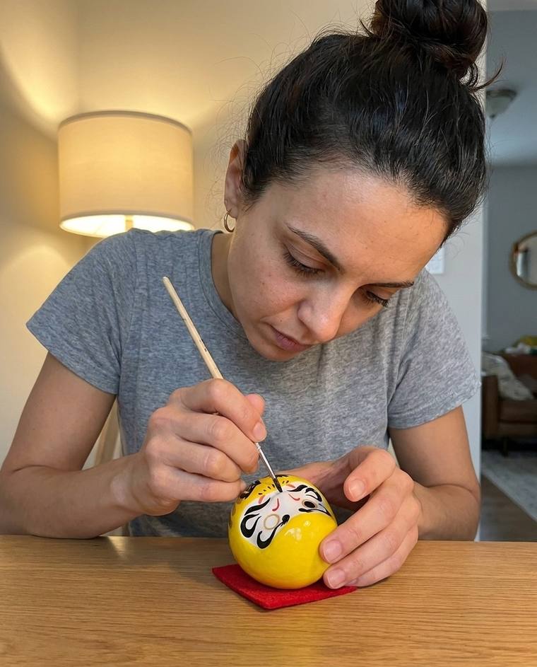 Emily filling in the first eye of a yellow Daruma at the kitchen sink