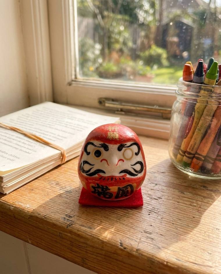 A red one-eyed Daruma on the windowsill above Patricia's kitchen sink