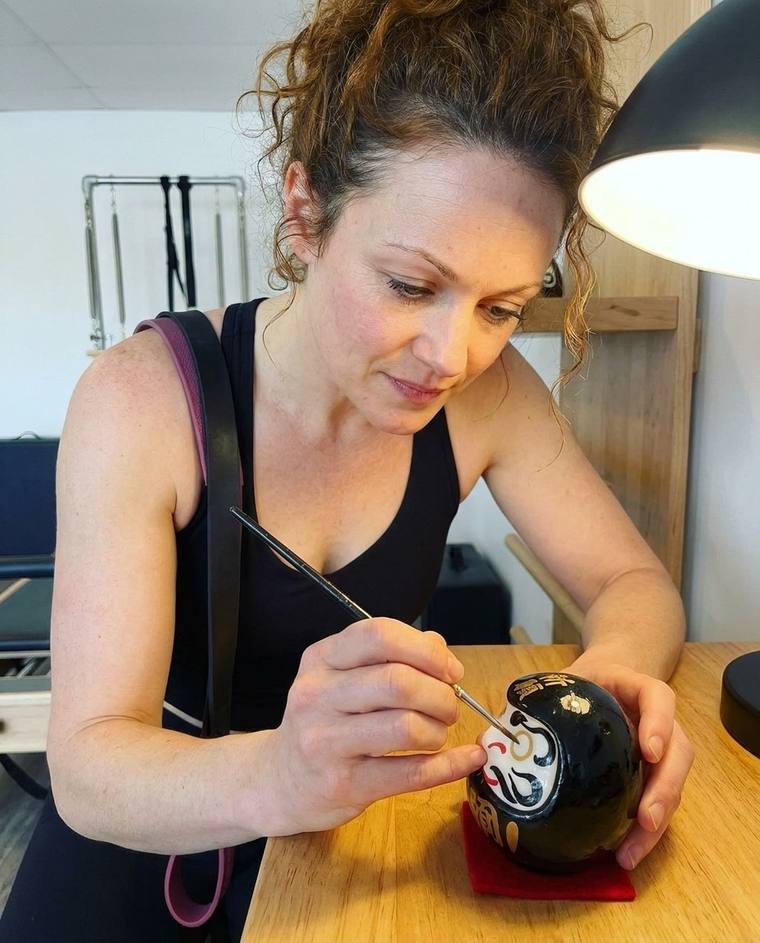 Hannah painting the first eye of a black Daruma on her kitchen counter