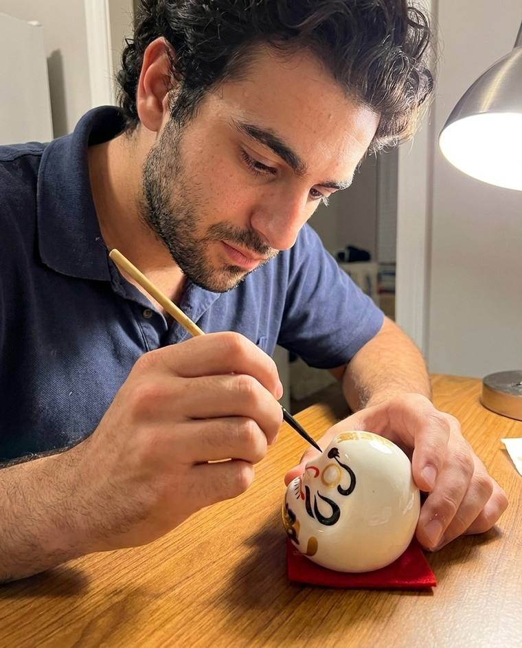 Jack painting the first eye of a white Daruma at his kitchen table