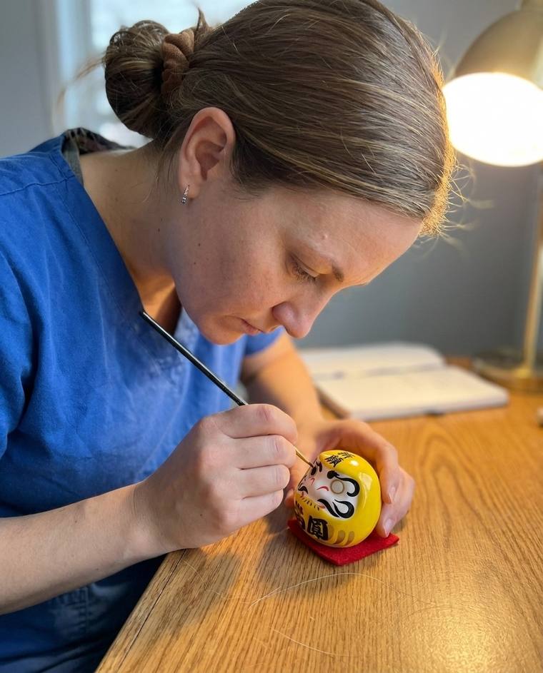 Natalie filling in the first eye of a yellow Daruma at her kitchen sink