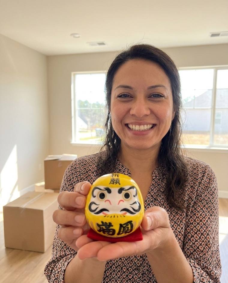 Tanisha painting the second eye of the yellow Daruma on the floor of her empty new living room
