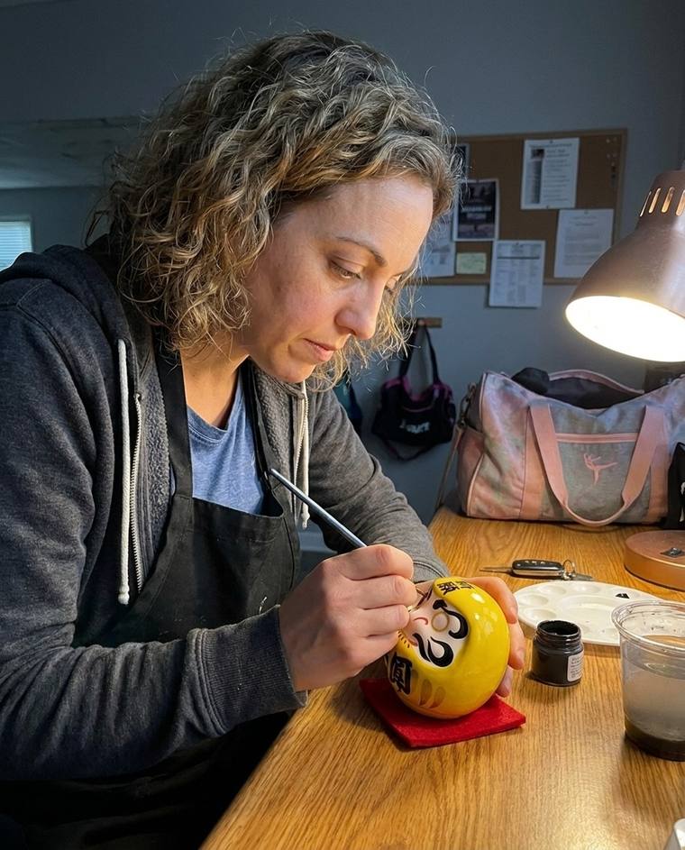 Mariah painting the first eye of a yellow Daruma in the laundry room